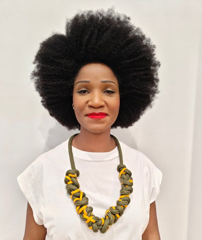Person with an afro wearing a chunky khaki green rope necklace, interwoven with yellow leather