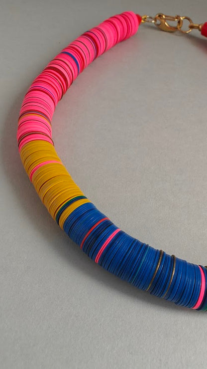Close up of a colorful necklace with pink, yellow, and blue circular beads on a gray background