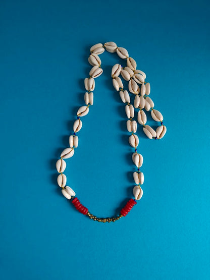 Necklace made of double backed cowrie shells, accents of brass and red recycle glass beads on a blue background