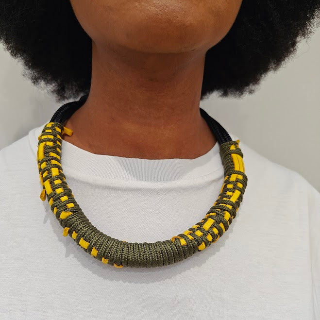 Person wearing a white top with a green and navy rope necklace with yellow leather weaving.